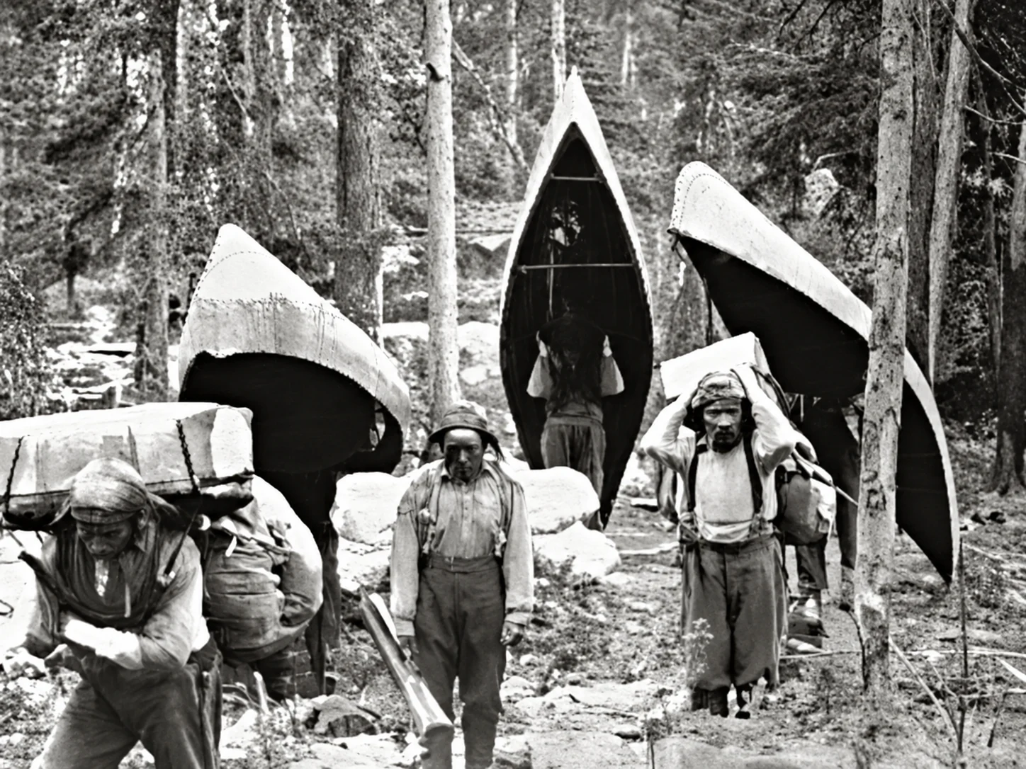 Indigenous travellers carrying canoes through a snowy forest
